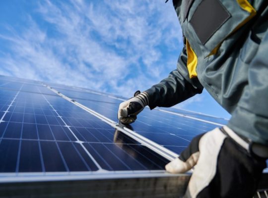 Close up of man technician in work gloves installing stand-alone photovoltaic solar panel system under beautiful blue sky with clouds. Concept of alternative energy and power sustainable resources.